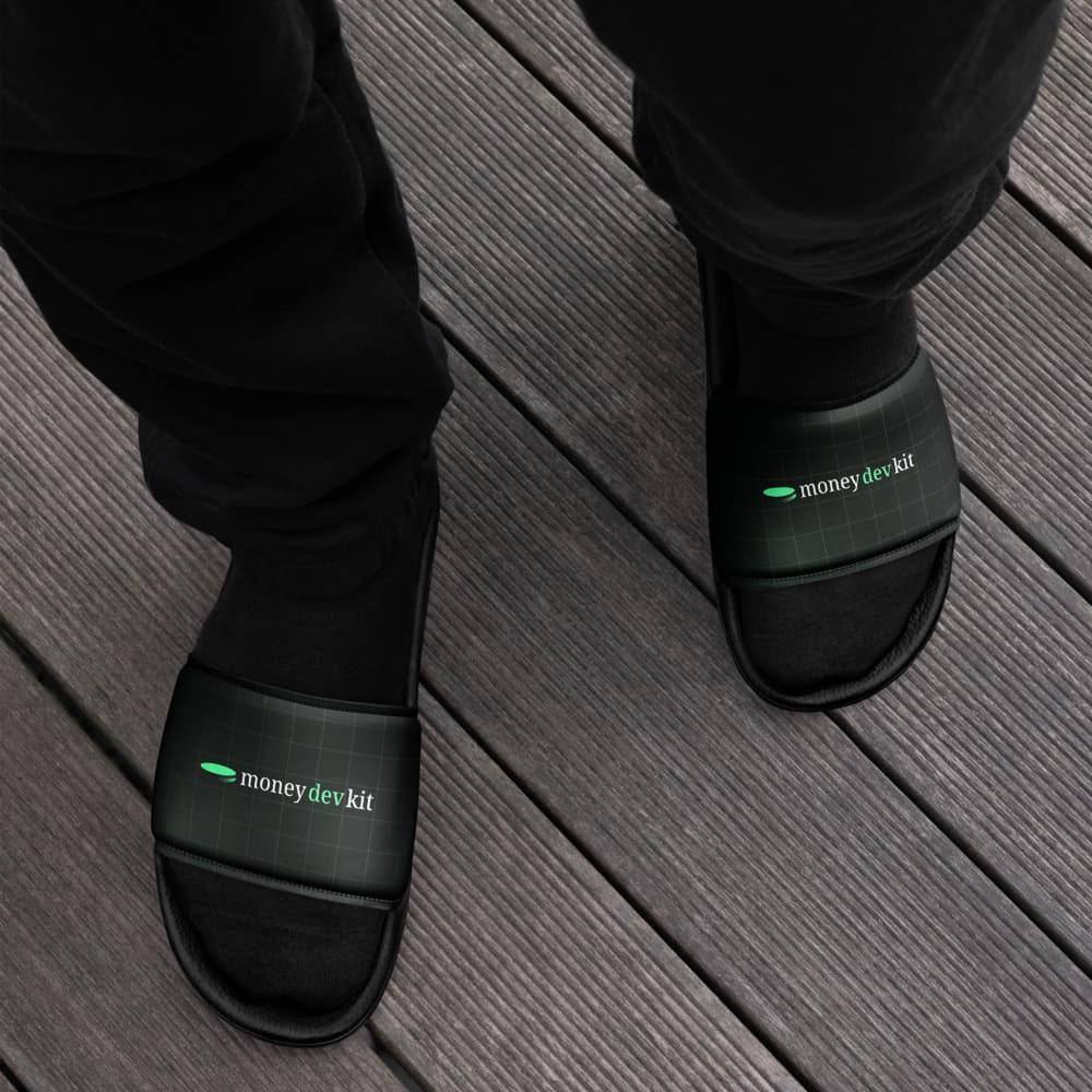 Black moneydevkit slides worn on a wooden deck, top-down view